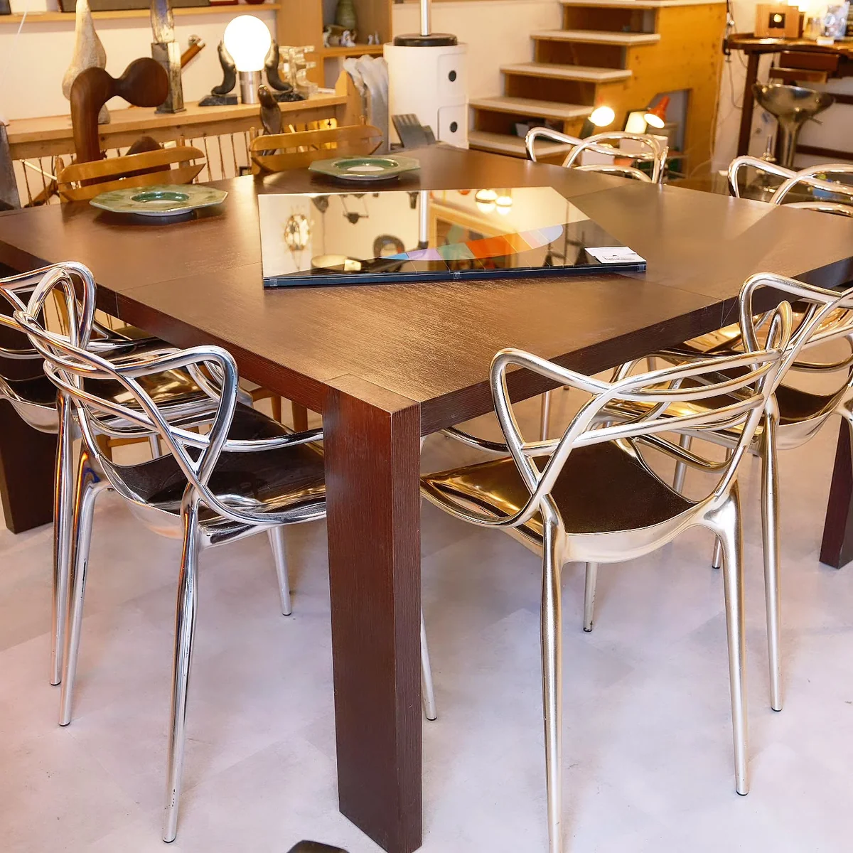 Table en bois sombre avec des chaises argentées dans un showroom de design vintage.