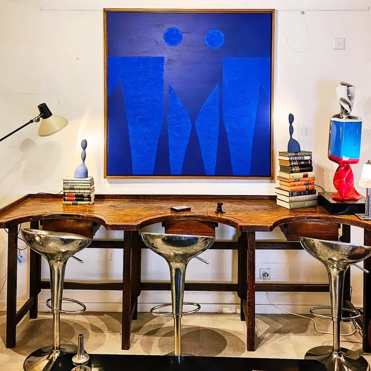 Bureau en bois, tabourets argentés, tableau bleu abstrait et objets décoratifs dans un showroom.