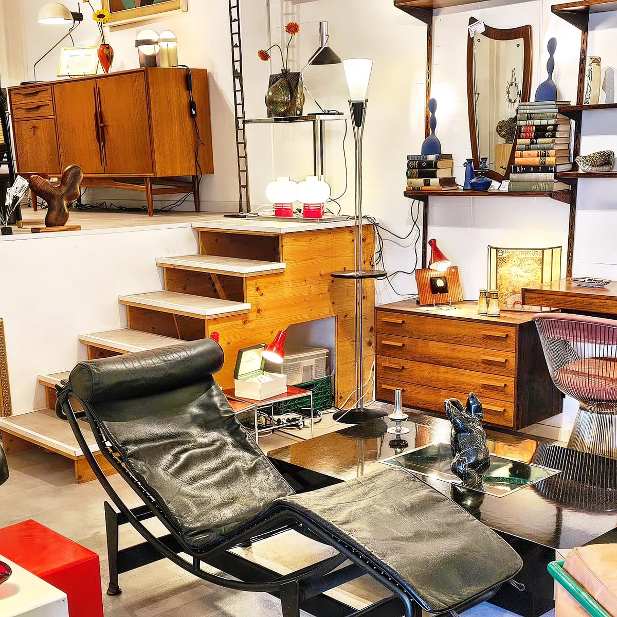 Salon de design vintage avec chaise longue en cuir noir, commodes en bois et lampes d'appoint.
