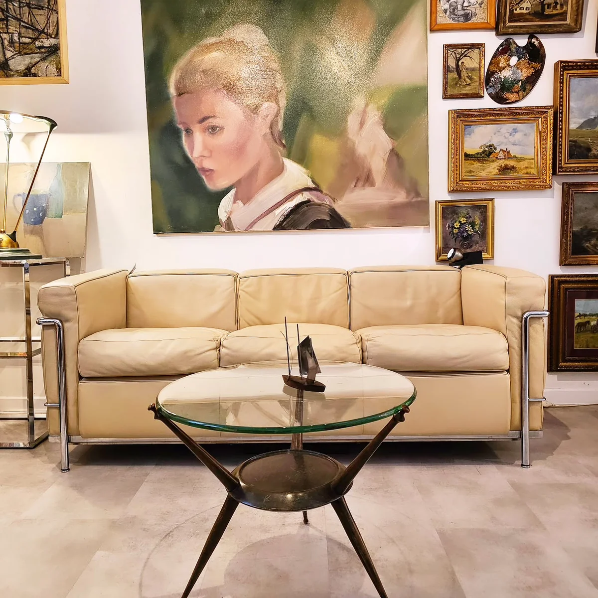Canapé en cuir beige devant une table basse en verre et métal, avec des tableaux accrochés au mur.