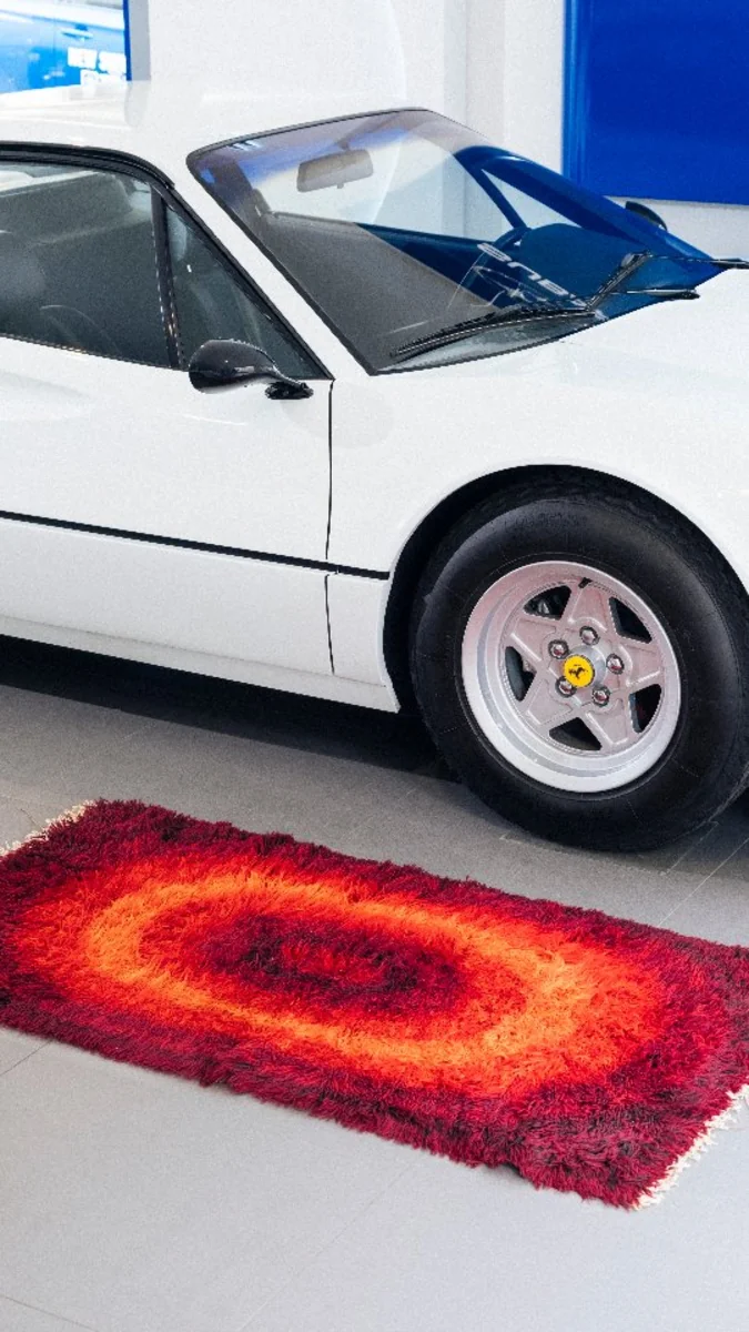 Gros plan sur une voiture de sport blanche avec un tapis rond aux couleurs vives posé devant.