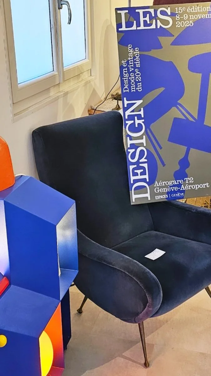 Un fauteuil en velours bleu nuit à côté d'un objet design et d'une affiche pour un évènement design