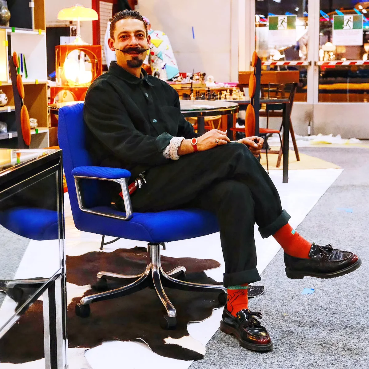 Malek Youssef, fondateur de Cyclup Design, installé dans un fauteuil bleu vif au milieu de meubles vintage.