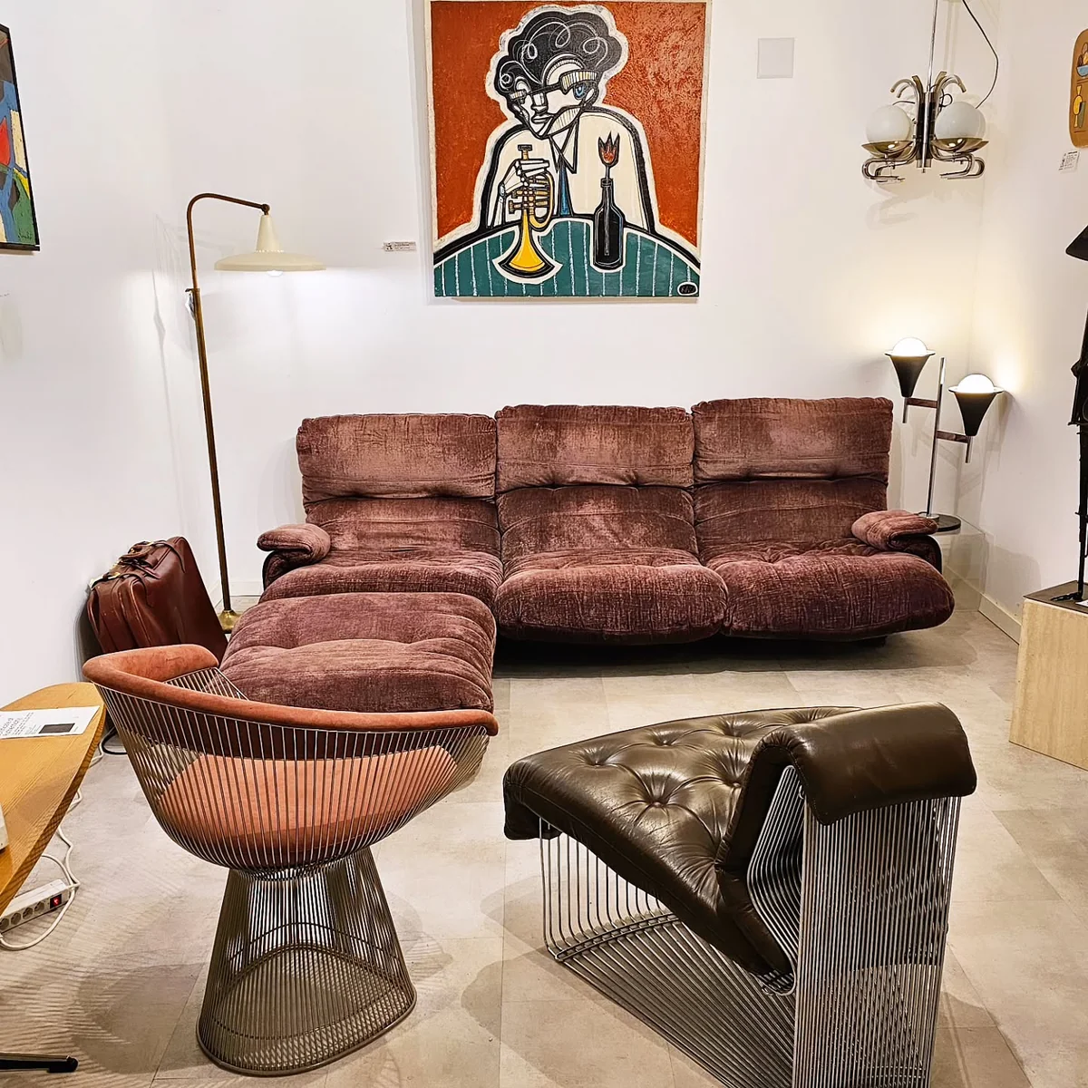 Vue d'un salon vintage avec canapé rose poudré, fauteuil design et tableau abstrait.