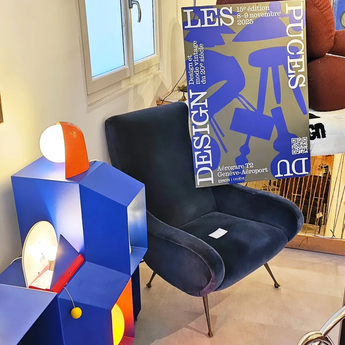 Affiche et mobilier design dans un showroom, avec un fauteuil bleu et une table basse lumineuse.