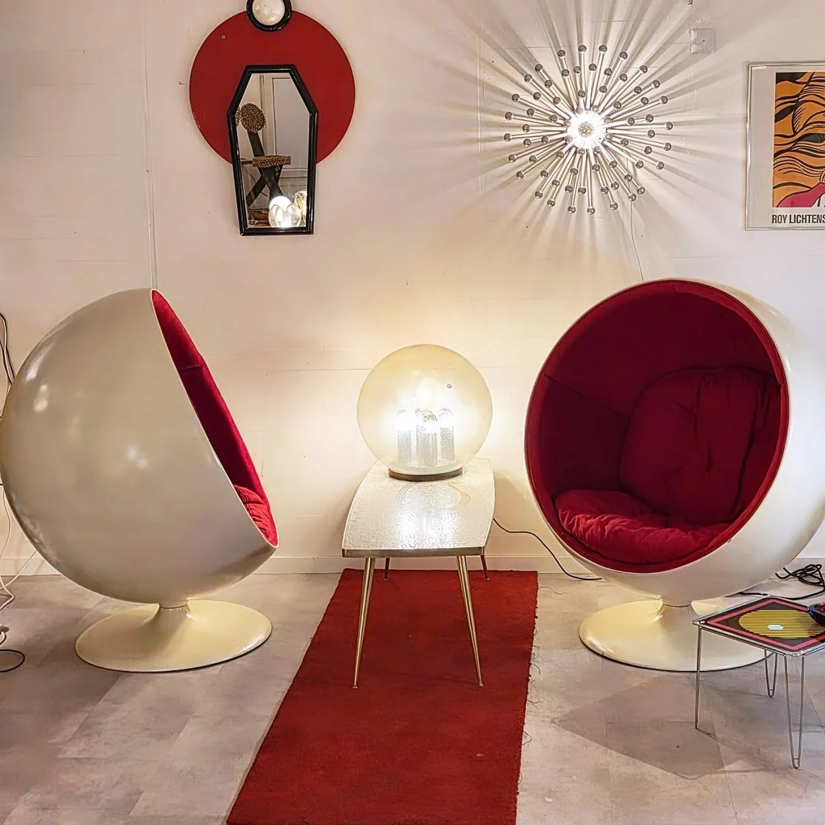 Deux fauteuils oeuf rouges et blancs, un miroir geometrique et luminaires eclatants dans le showroom.
